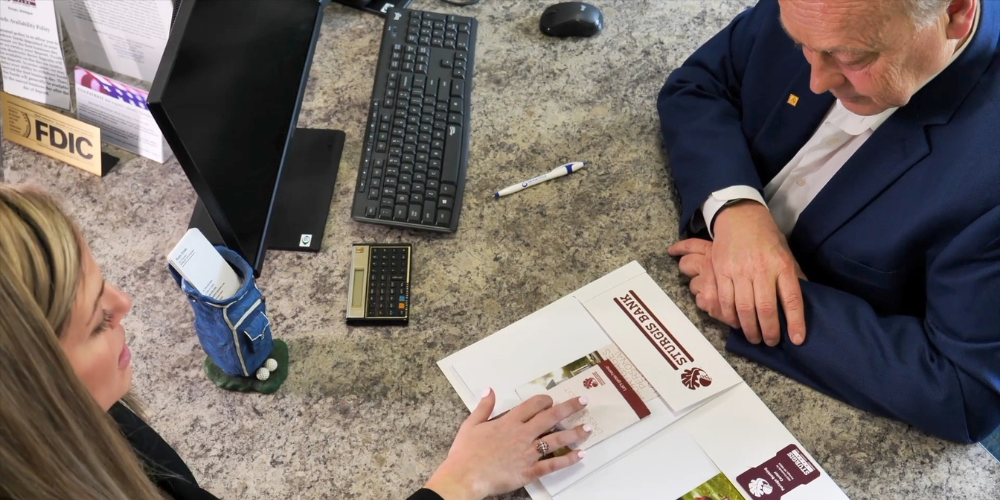 A Sturgis Bank employee reviews banking materials with a customer at a branch counter.